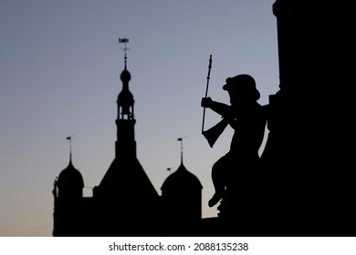 A silhouette of a Putto, a small statue of a child, blowing a horn on the Wilhelmina fountain in Deventer, the Netherlands. In the background the silhouette of the old weighing house can be seen.