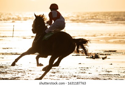 Silhouette of race horse and jockey racing racing into the sun on the beach, wild Atlantic way on the west coast of Ireland