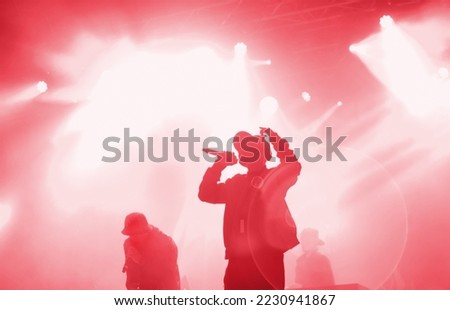 Silhouette of rap band performing on concert stage in bright red lights. Unrecognizable young rapper singing on concert