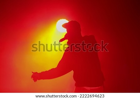 Silhouette of rap singer with microphone. Cool rapper with mic in hand singing on concert stage in bright red lights. Hip hop artist performing live on scene in music hall. Party poster template