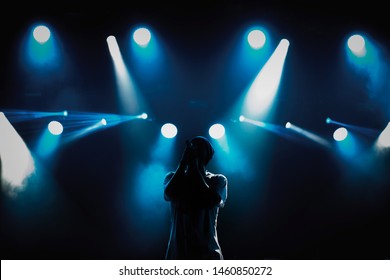 Silhouette Of Rap Singer Performing On Concert Stage In Bright Lights. Musician With Microphone In Hands Singing On Music Festival In Night Club. Rapper Performs Live Set On Scene