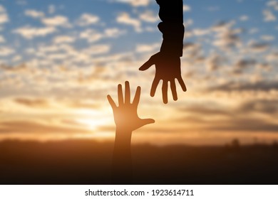 Silhouette Of Reaching, Giving A Helping Hand, Hope And Support Each Other Over Sunset Background. Help Concept