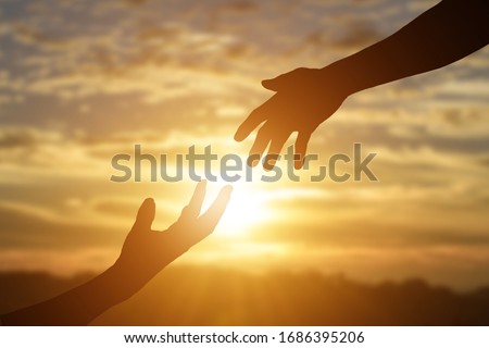 Silhouette of reaching, giving a helping hand, hope and support each other over sunset background. 