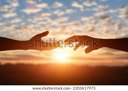 Silhouette of reaching, giving a helping hand, hope and support each other over sunset background. Help, friendship international day concept.