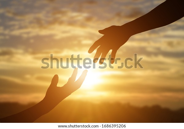 Silhouette of reaching, giving a\
helping hand, hope and support each other over sunset background.\
