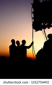 Silhouette of riggers working with mobile crane in the oilfield at sunset
