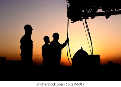Silhouette of riggers working with mobile crane in the oilfield at sunset
