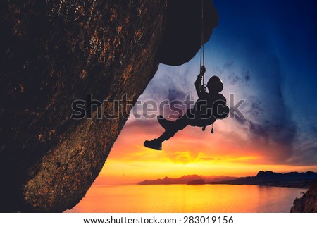 Silhouette of rock climber climbing an overhanging cliff with sunset over the sunset on a sea background