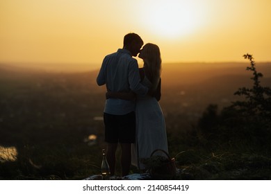 Silhouette of romantic couple kissing while standing on a hill at evening sunset. Happy gorgeous elegant couple kissing on summer picnic. - Powered by Shutterstock