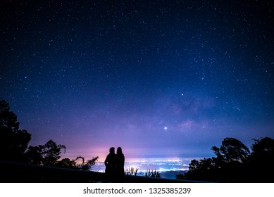 Silhouette Of Romantic Couple Watching Milky Way And City Light At Night