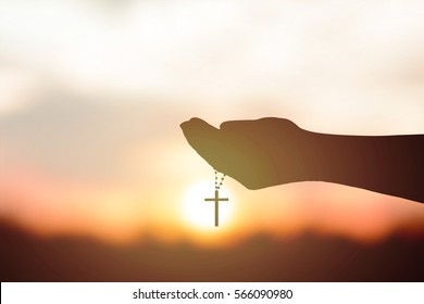 Silhouette rosary against cross in hand. Background sunrise - Shutterstock ID 566090980