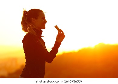 Silhouette Of Runner Woman Eating Energy Bar After Running At Sunset In The Mountain