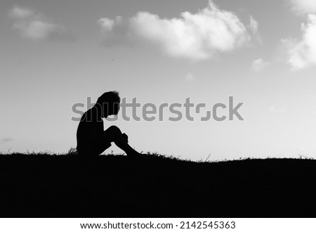 Silhouette of sad little boy child alone sitting with face down. 