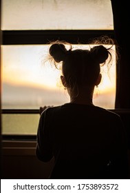 The silhouette of the sad little girl with double hair buns looking outside the train window