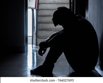 Silhouette of a sad young man sitting in the dark leaning against the wall with his back, The sun is in sorrow.