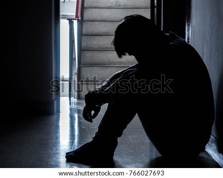 Silhouette of a sad young man sitting in the dark leaning against the wall with his back, The sun is in sorrow.