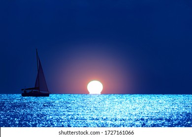 Silhouette Of A Sailing Boat On Open Sea With Moonlight Twinkling Water.