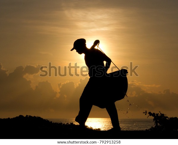 Silhouette of a salt farmer carrying\
homemade yoked baskets to collect sea water as part of the natural\
gourmet salt production process, Kasumba,\
Bali