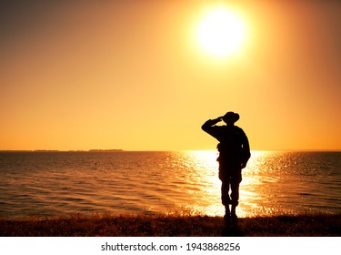 Silhouette of saluting commando soldier, army infantryman standing on shore during sunset or sunrise. Military solemn ceremony, respectable salute for honoring fallen heroes and comrades veterans