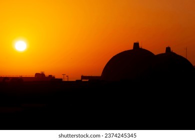 Silhouette of San Onofre nuclear power plant main reactors at sunset with sun visible.