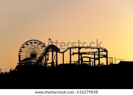 silhouette of santa monica pier amusement park with ferris wheel at sunset as seen form the beach