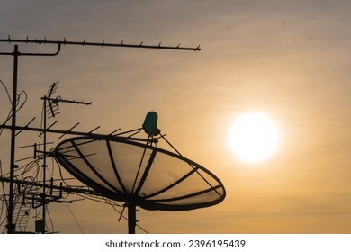 Silhouette of satellite dish on the roof for communication and television on beautiful sunset sky with copy space. - Shutterstock ID 2396195439