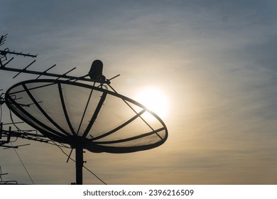 Silhouette of satellite dish on the roof for communication and television on beautiful sunset sky with copy space. - Shutterstock ID 2396216509