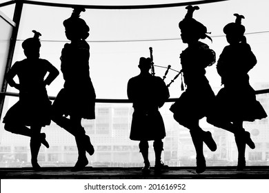 Silhouette Of Scottish Highland Dancing Group Dancers Dancing To A Bagpipe Music. Real People. Copy Space