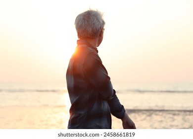 The silhouette of senior Asian man walking along the beach in the evening time - Powered by Shutterstock