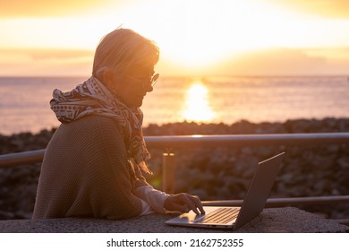 Silhouette Of Senior Business Woman Close To The Beach Using Laptop. Elderly Female In Remote Work Enjoying Orange Sunset At Sea, Horizon Over Water