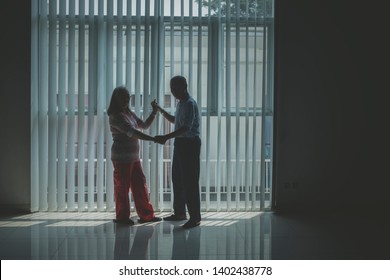 Silhouette Of Senior Couple Looking At The Camera While Dancing Near The Window. Shot In The Dark Room 