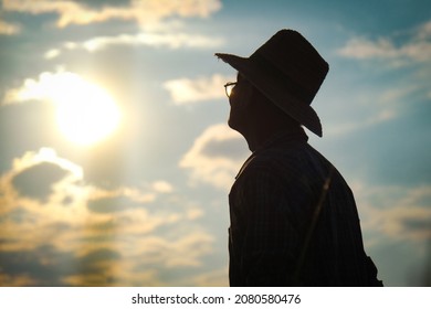 Silhouette of Senior farmer standing in rice field at sunset. An elderly man in a hat looking into the distance on a golden sky background.