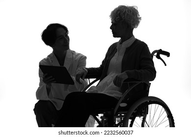 Silhouette of a senior woman in a wheelchair and a man who talks with her. - Powered by Shutterstock