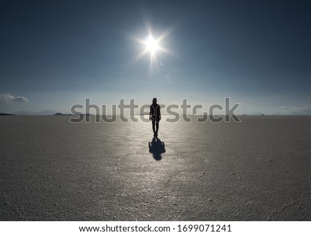 Silhouette and shadow of a person facing the sun and walking into the light in bright sunshine and blue sky in the vastness of the dry Salt Flats of Uyuni, Bolivia. Back shot.
