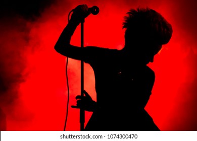 Silhouette of short haired female singer in black and red colours. Performer holding microphone and microphone stand.