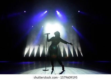 Silhouette of singer on stage. Dark background, smoke, spotlights