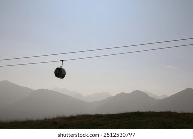 silhouette of a single cable car with a monochrome background of hazy mountains - Powered by Shutterstock