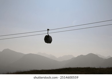 silhouette of a single cable car with a monochrome background of hazy mountains - Powered by Shutterstock