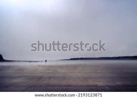 Silhouette of a single man walking alone on a foggy beach