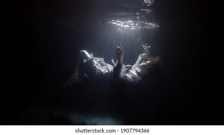 Silhouette Of Sinking Woman Underwater, Floating And Diving Under Surface Of Dark Pool