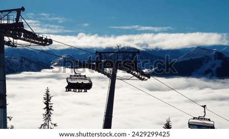 Silhouette of ski lift in a Ski Resort and beautiful sight of alps with lower clouds underneath a clear blue and sunny sky. Lots of fog and mist in the valley of Westendorf, Austria (Tirol).