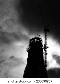 Silhouette of a skyscraper under construction with a tower crane perching at its peak against a stormy cloudy sky,
