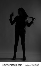 The Silhouette Of A Slender Woman With A Gun In Darkness