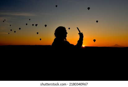 Silhouette Of Smart Phone In Hands Of Woman Taking Pictures Of A Beautiful Landscape And Balloons In Cappadocia. Sunrise Time, Dreamy Travel Concept