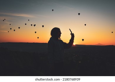 Silhouette Of Smart Phone In Hands Of Woman Taking Pictures Of A Beautiful Landscape And Balloons In Cappadocia. Sunrise Time, Dreamy Travel Concept