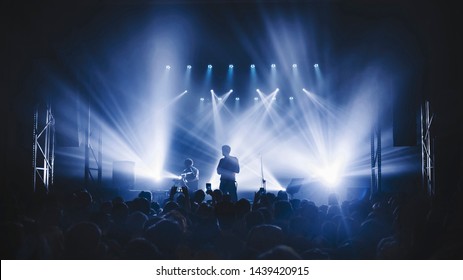 Silhouette Of The Soloist Standinf In A Fog In The Rays Of Light. Concert Crowd In Front Of Bright Stage Lights. Dark Background, Smoke, Concert  Spotlights