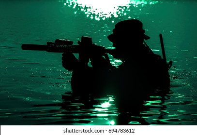 Silhouette Of Special Forces With Rifle In Action During Night Raid Crossing River In The Jungle Waist Deep In The Water. Moon Path Glowing