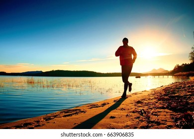 Silhouette Of Sport Active Adult Man Running And Exercising On The Beach. Calm Water, Island And Sunset Sky Background.