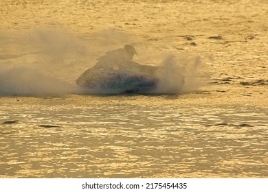 Silhouette Sport Man Riding His Jet Ski And Water Spray On Sunset Background.Jet Ski Racing Competition And Water Splash.Extreme Outdoor Water Sport Concept.