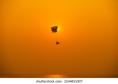 Silhouette of the sport Paramotor control flying through soft sunlight orange sunset sky